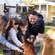 A family of 4 reaching over a wooden fence to pet alpacas at an outdoor animal area with picnic tables